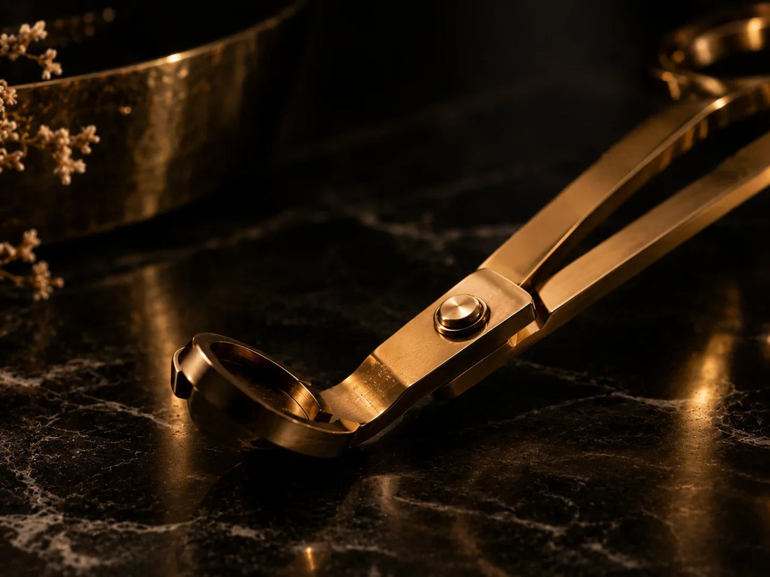 Goldener Kerzendochtschneider in Nahaufnahme auf schwarzem Marmor mit feinen Maserungen und warmen goldenen Lichtreflexionen. Die dunkle, elegante Inszenierung unterstreicht die hochwertige Ästhetik des Kerzenzubehörs.